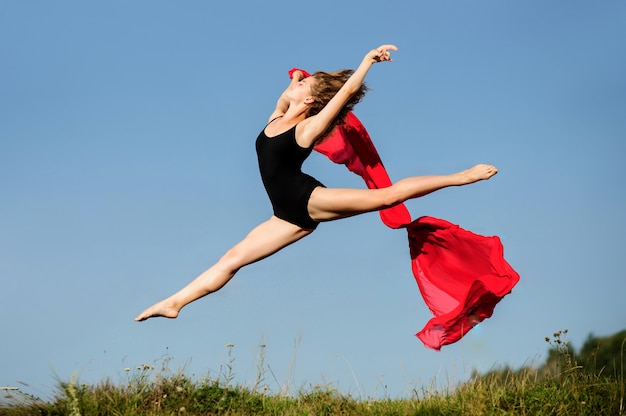 Zdjęcie profesjonalny tancerz skoki z czerwonej tkaniny na zachód słońca.