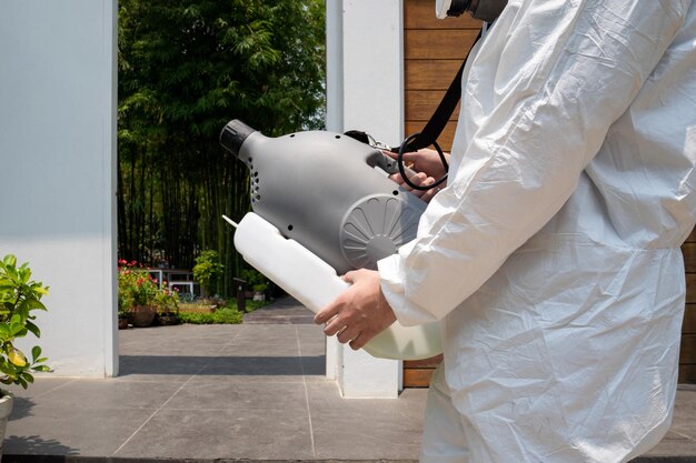 Profesjonalny technik w kombinezonie prewencyjnym ze sterylizatorem i dezynfekcją sprayów wodnych na polu zewnętrznym w celu oczyszczenia z koronawirusa COVID19