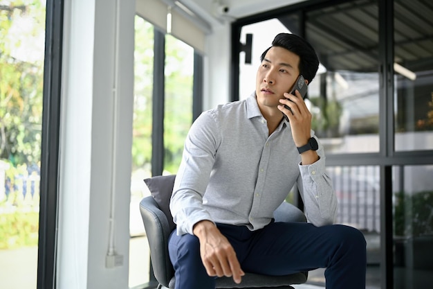 Profesjonalny, tysiącletni azjatycki biznesmen rozmawia przez telefon, siedząc w biurze