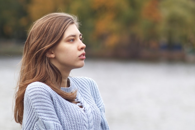 Profil boczny portret poważnej zamyślonej zamyślonej młodej kobiety w jesiennym parku w pobliżu jeziora w sweter z dzianiny, patrząc w dal