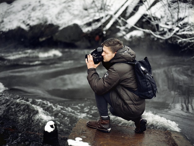 Zdjęcie profil mężczyzny fotografującego kamerą na brzegu rzeki w zimie