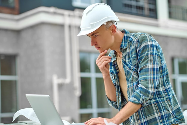 Profil mężczyzny patrzącego na laptopa na placu budowy