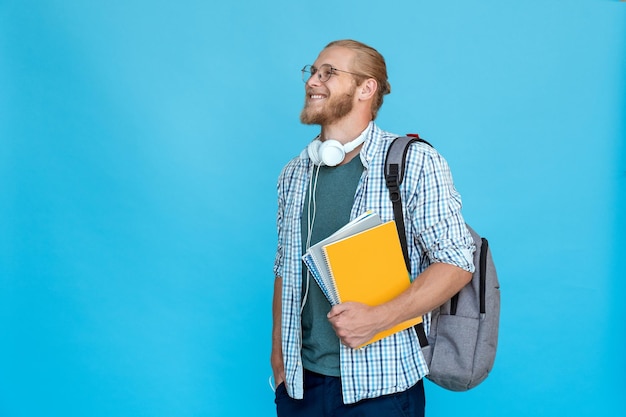 Profil młodego brodatego studenta college'u trzyma plecak z notatnikami i patrzy na przestrzeń