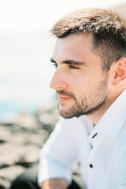 Profil młodego mężczyzny w białej koszuli siedzącego nad morzem
