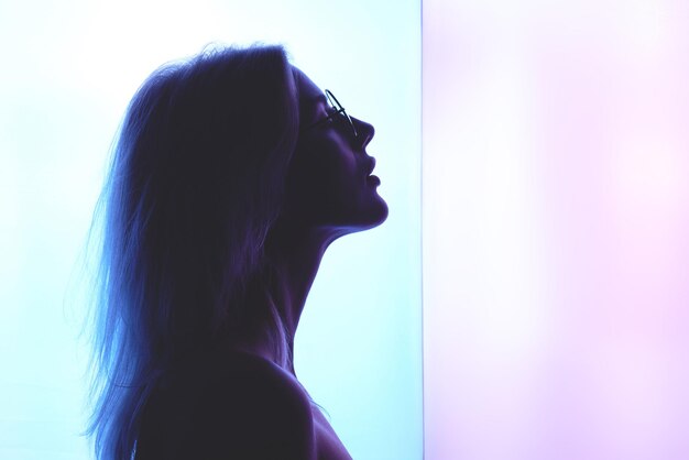 Profil pięknej młodej blond kobiety w okularach na tle niebieskiego różowego światła