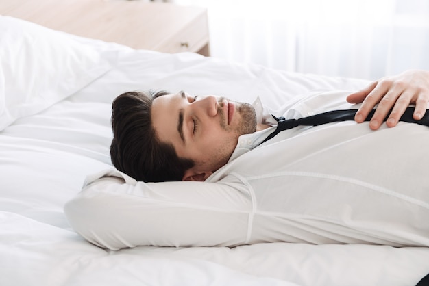 profil zrelaksowanego brodatego biznesmena noszącego oficjalne ubrania z zamkniętymi oczami na łóżku w apartamencie hotelowym