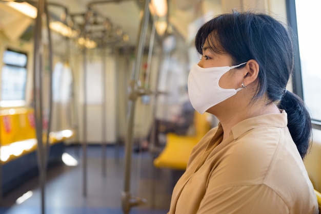 Profilowy widok z nadwagą Azjatycka kobieta z maskowym obsiadaniem z odległością wśrodku pociągu