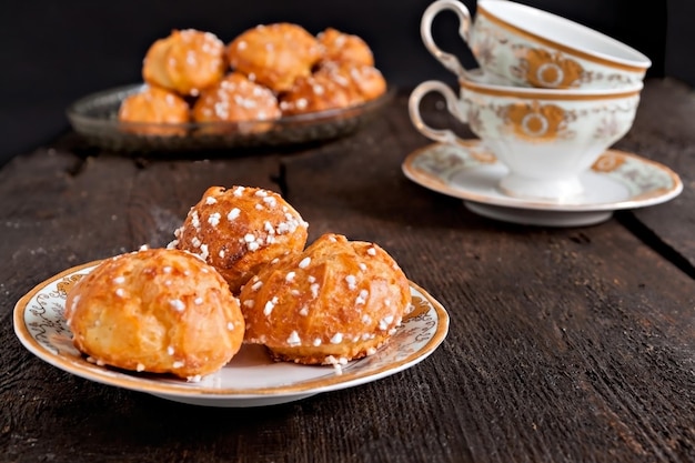 Profiteroles zwieńczona cukrem i vintage filiżanka z herbatą na ciemnym tle