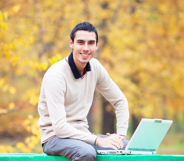 Programista z notebookiem siedzący w jesiennym parku