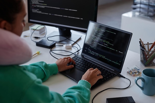 Programistka siedzi w miejscu pracy z komputerami i pisze kody na laptopie w biurze