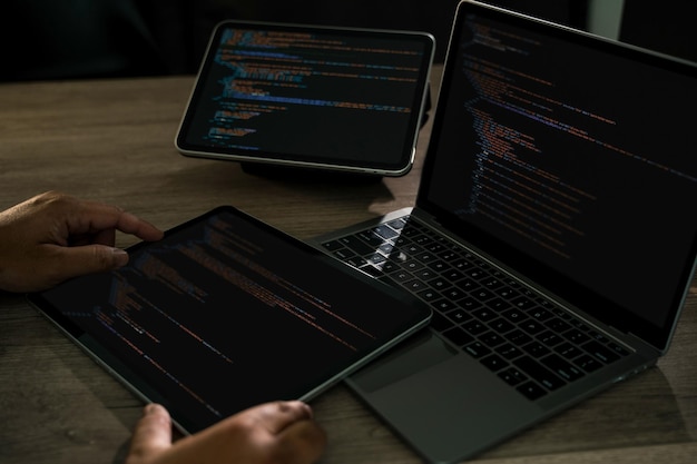 Programmer writing Development Website design code at a desk with laptop and tablet dark workspace hands on keyboard css and html modern software development tech projects