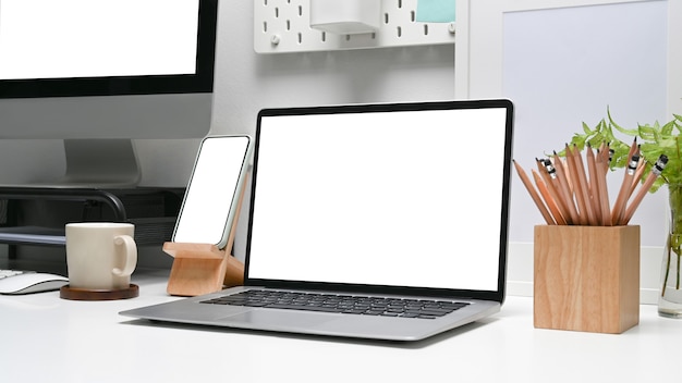 Projektant miejsca pracy z komputerem laptop i inteligentny telefon z pustym ekranem na białym biurku.