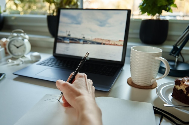 Projektant rysuje szkic na papierze siedzi przy biurku z laptopem przed oknem
