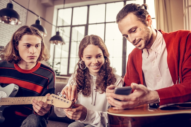 Promieniejąca dziewczyna. Rozpromieniona kręcona ciemnowłosa dziewczyna czuje radość podczas nauki gry na gitarze