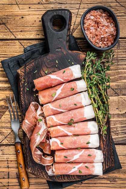 Prosciutto crudo Suszona szynka parmeńska na drewnianej desce do krojenia z tymiankiem. drewniane tła. Widok z góry.