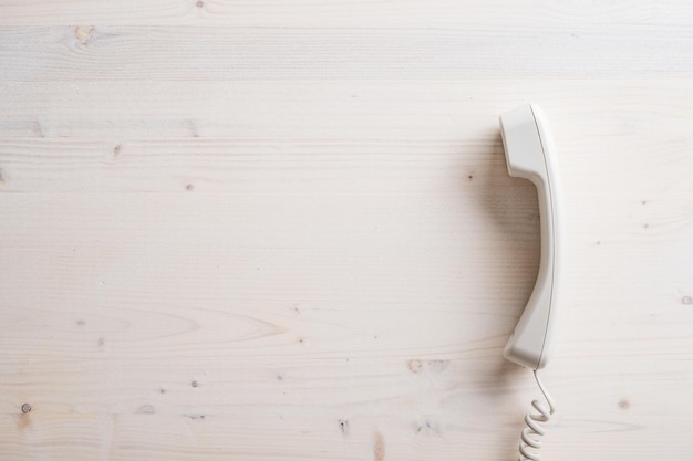 Prosta biała słuchawka telefonu stacjonarnego umieszczona na prostym drewnianym tle