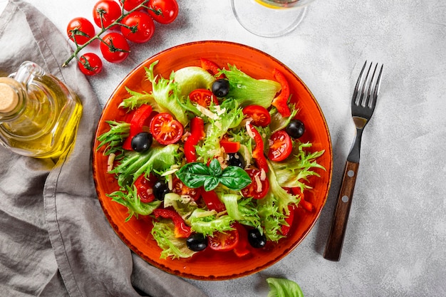 Prosta letnia sałatka z sałaty, pomidorów z oliwkami i oliwą z oliwek na czerwonym talerzu widok z góry.