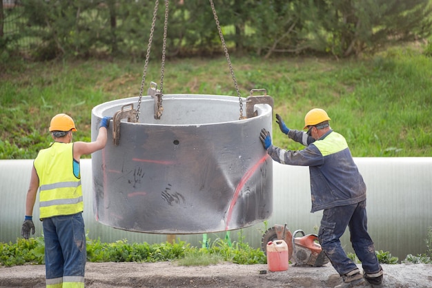 Przebudowa odcinka drogi z ułożeniem miejskich rur kanalizacyjnych Pracownicy montują betonowe rury do kanalizacji Koparka podnosi betonowy pierścień przed wkopaniem w ziemię