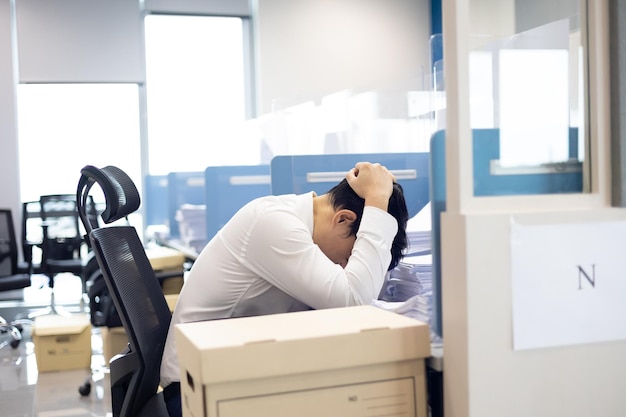 Przeciążony pracownik biurowy Azjatycki pracownik biurowy odczuwa ból głowy i jest zestresowany dużą ilością dokumentów na biurku w biurze