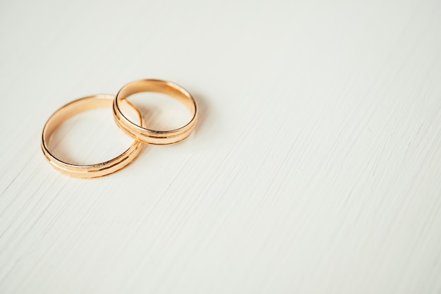 Przecinające ślubne złote pierścienie w lewej części białego drewnianego tła