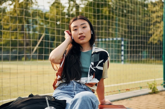 Przeciwko siatce boiska Młoda azjatycka kobieta jest na zewnątrz w ciągu dnia