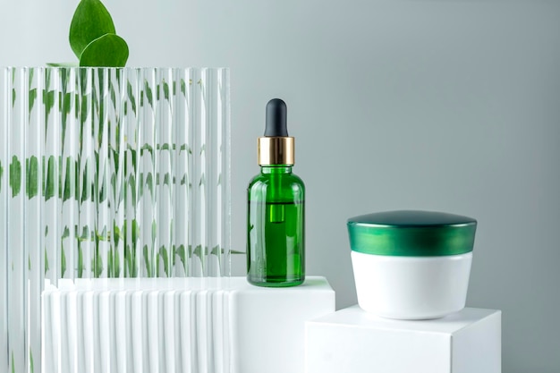 Przeciwstarzeniowe kolagenowe serum do twarzy w zielonej szklanej butelce i krem do twarzy na białym podium z przestrzenią do kopiowania Koncepcja naturalnego organicznego kosmetycznego piękna