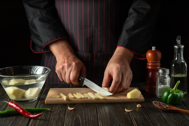 Przed przygotowaniem dania narodowego szef kuchni kroi nożem surowe ziemniaki na małe kawałki Zbliżenie rąk kucharza podczas pracy w kuchni