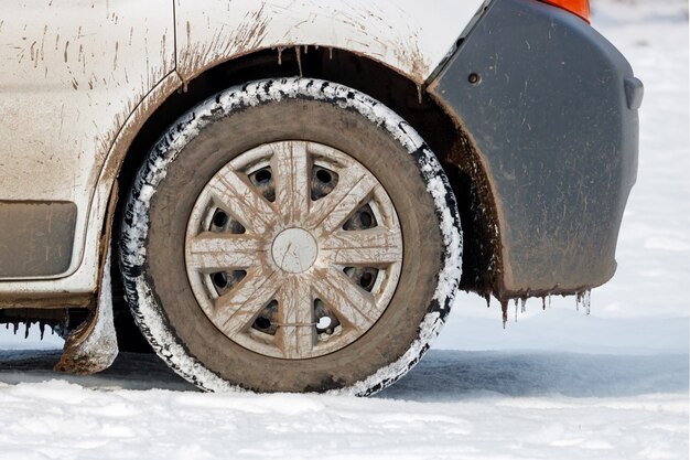 Przednie koło brudnego samochodu stojącego na śniegu z bliska