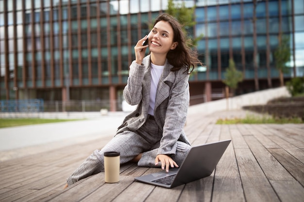 Przedsiębiorca bizneswoman mówiący na smartfonie i przeglądający laptopa na zewnątrz