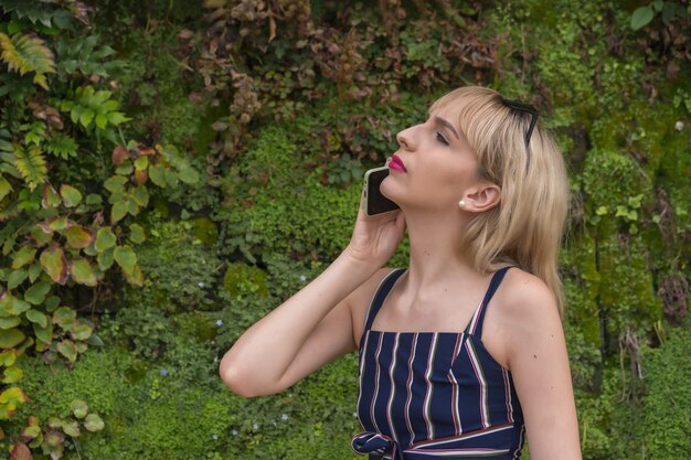 Przedsiębiorca dziewczyna w parku biznesowym na zielonej ścianie roślin, młoda blondynka nawiązująca połączenie z telefonem, skopiuj i wklej spację