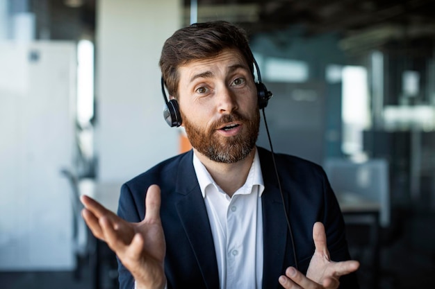 Przedsiębiorca w średnim wieku w słuchawkach gestykuluje patrząc na kamerę internetową komputera podczas rozmowy wideo w biurze
