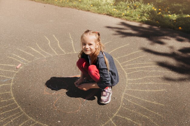 Przedszkolak rysuje kredą na asfalcie latem w parku