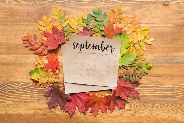 Zdjęcie przegląd kalendarza wrześniowego w otoczeniu kolorowych jesiennych liści na drewnianym