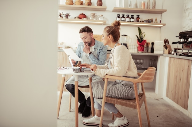 Przeglądanie biografii. Skoncentrowany mąż i żona siedzący przy laptopie szukający siły roboczej do rodzinnej kawiarni.