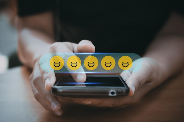 Przejrzyj ocenę i opinie najlepsze i doskonałe podziwianie przez recenzenta z bliska na dłoni klienta naciskającej na ekranie smartfona ze złotymi twarzami emoji