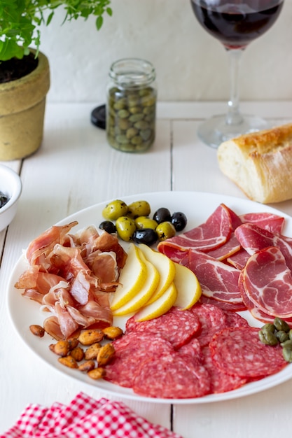 Przekąska do wina. Prosciutto, szynka parmeńska, salami, migdały, oliwki, bagietka. Antipasti