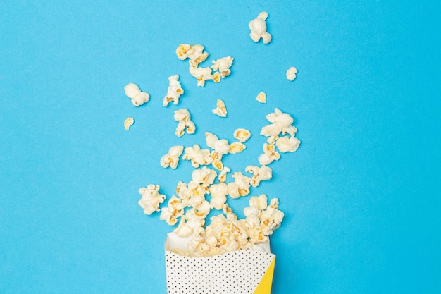 Przekąska z oglądania koncepcji filmu Słodki popcorn unosi się z papierowego kubka na jasnoniebieskim tle