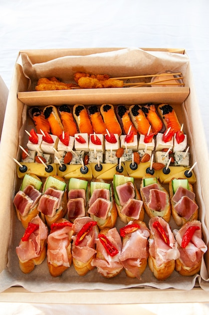 Przekąski w kartonie z małymi kanapkami, eklerkami, bruschettą z wędlinami, serem i owocami morza na bufet cateringowy na imprezę.
