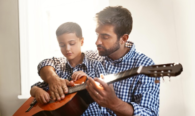 Przekazywanie daru muzycznego Ujęcie młodego mężczyzny grającego na gitarze z synem w domu