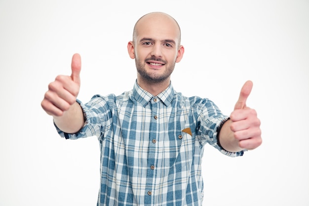 Przekonany, uśmiechnięty młody człowiek w kraciastej koszuli pokazujący kciuki do góry obiema rękami nad białą ścianą