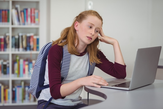 Przemyślana uczennica za pomocą laptopa w bibliotece