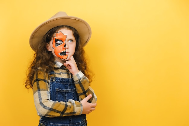 Przemyślane Dziecko Dziewczynka Z Maską Do Makijażu Halloween Zastanawia Się Nad Decyzją, Myśląc O Czymś, Pozowanie Na Białym Tle Nad żółtą ścianą Studyjną Z Miejsca Na Kopię. Hmm Coś Dziwnego