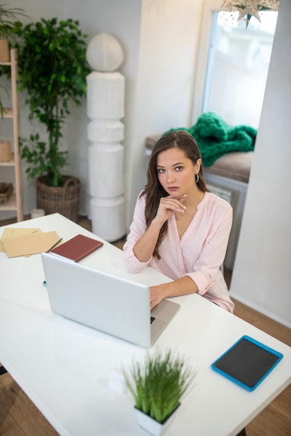 Przemyślany inteligentny bizneswoman siedzi przy biurku podczas pracy