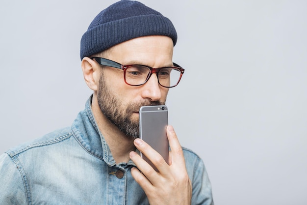 Przemyślany mężczyzna w średnim wieku z zarostem trzyma inteligentny telefon w pobliżu ust, głęboko zamyślony, myśli o przyszłych planach izolowanych na białym tle Ludzie emocje koncepcja technologii