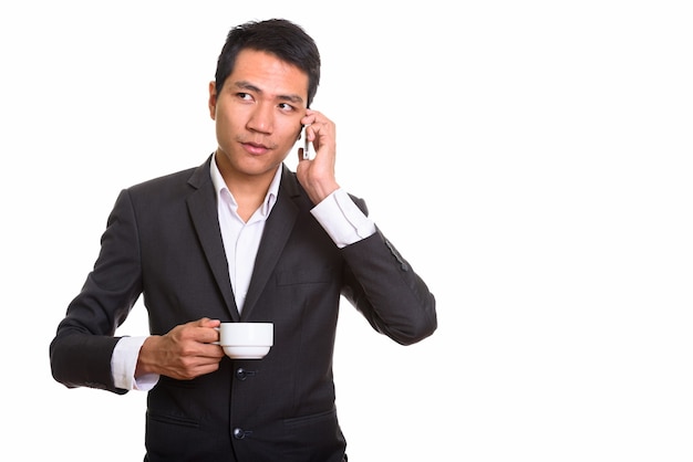 Przemyślany młody biznesmen azjatyckich rozmawia przez telefon komórkowy podczas picia kawy