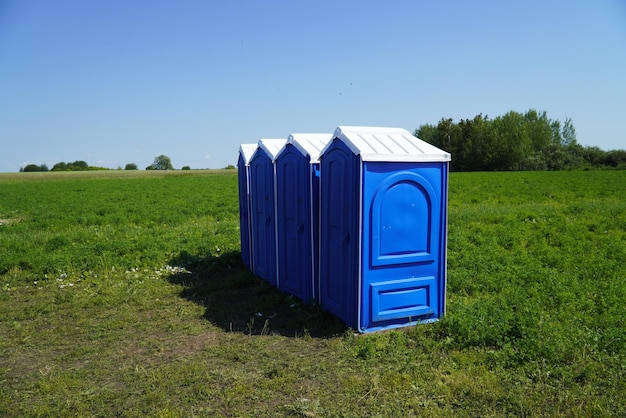 Przenośne plastikowe toalety w terenie na trawie na tle błękitnego nieba