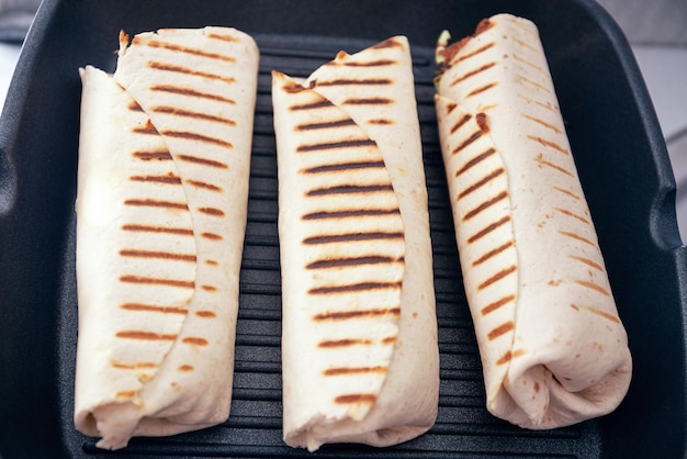 Przepis na shawarmę lub kebab wrap wypełniony grillowanym mięsem i warzywami i zawinięty w flatbread Kebab wrap grillowany na patelni grillowej