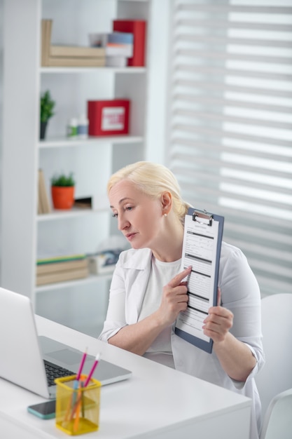 Przepis, poradnictwo online. Kobieta lekarz siedzi w miejscu pracy, pokazując receptę na ekranie laptopa, uważny poważny.