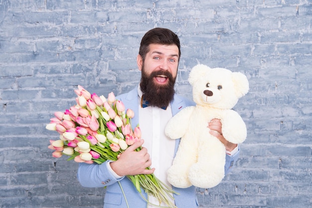 Przepraszam Dzień Kobiet Kocham Cię tak bardzo 8 marca Wiosenny prezent Brodaty mężczyzna hipster z kwiatami Brodaty mężczyzna z bukietem tulipanów i niedźwiedziem Data miłości międzynarodowe wakacje Miłość i romans