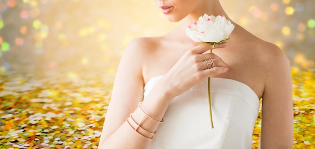 przepych, piękno, biżuteria i koncepcja luksusu - zbliżenie pięknej kobiety ze złotym pierścionkiem i bransoletką trzymającą kwiat na tle złotych świateł świątecznych